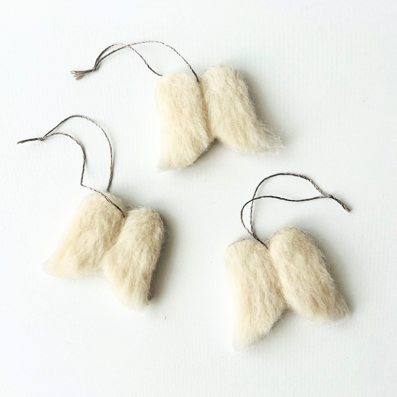 Három egyedi fehér gyapjú angyalszárny függődísz ezüst selyem zsinórral, egymás mellett fektetve, kézzel készült tűnemezelt részletekkel.