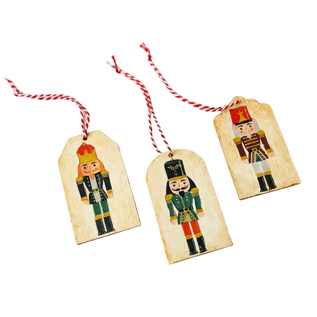 Három szines kézműves fa ajándékkísérő három különböző diótörő mintával, szalvéta technikával díszítve, piros-fehér pékzsineg akasztóval, egymás mellett fektetve.