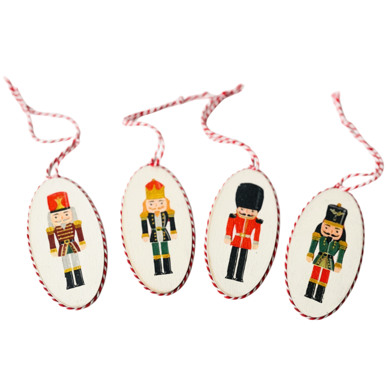 Négy kézműves, ovális fa karácsonyfadísz különböző diótörő mintákkal, szalvéta technikával díszítve, piros-fehér pékzsineg akasztóval, egymás mellett fektetve.