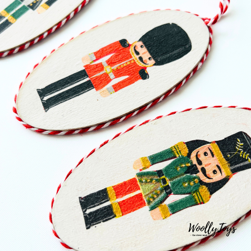 Közelkép egy kézműves diótörő mintás fa karácsonyfadíszről, amelyen jól látszik a szalvéta technika részletessége és a természetes fa erezete.