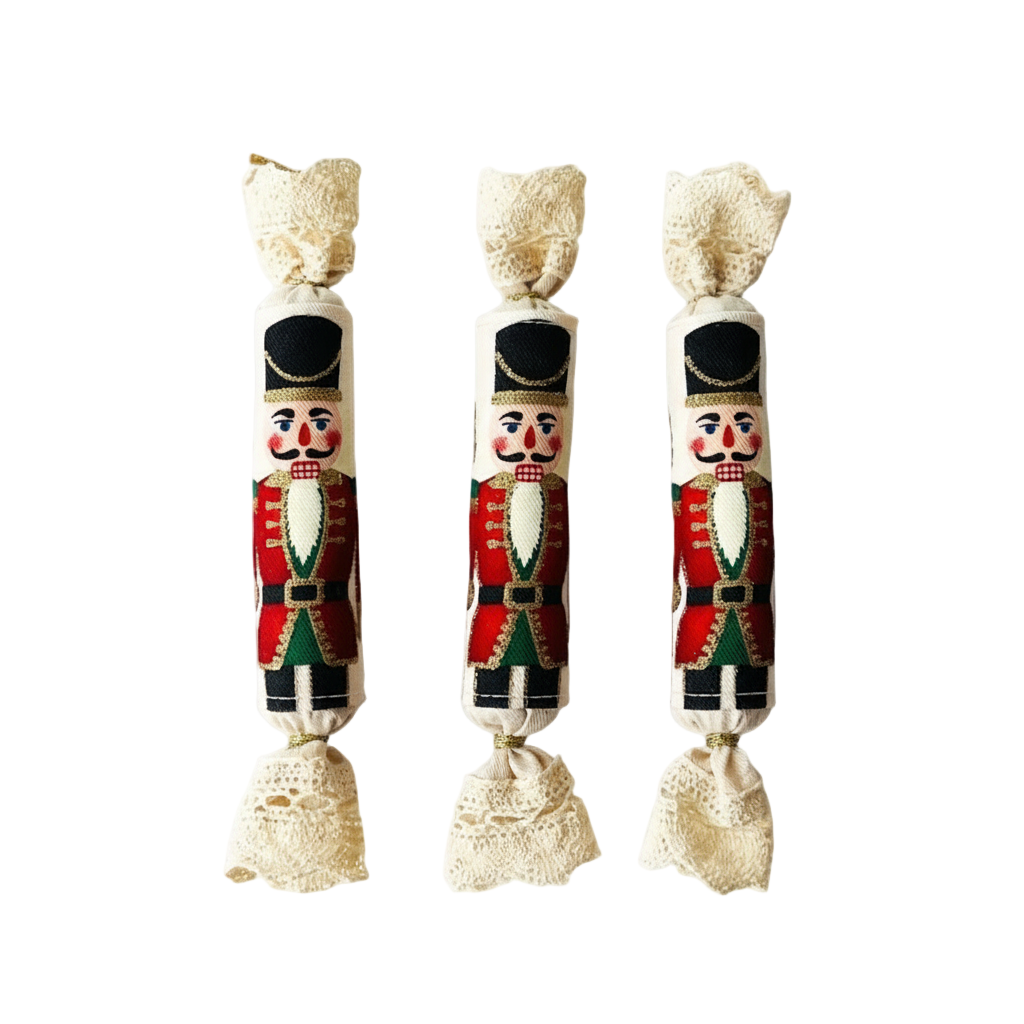 Három kézműves textil szaloncukor karácsonyfadísz fekete kalapos diótörő mintával, egymás mellett sorakozva, arany zsinórral.