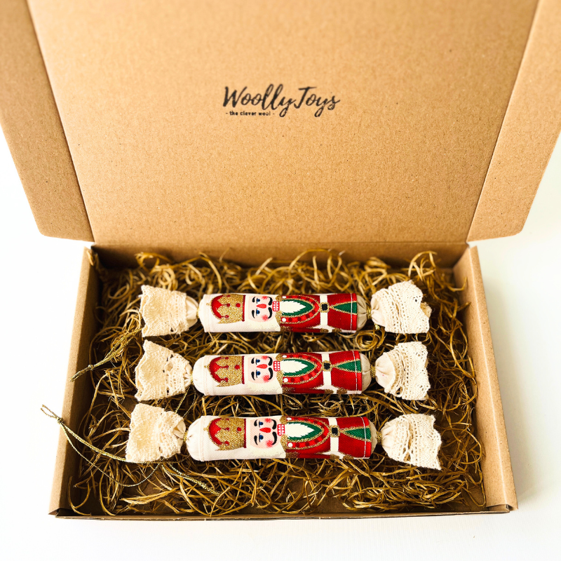 Három kézműves textil szaloncukor karácsonyfadísz piros kalapos diótörő mintával, elegáns kraft karton díszdobozban, ajándékozásra készen.