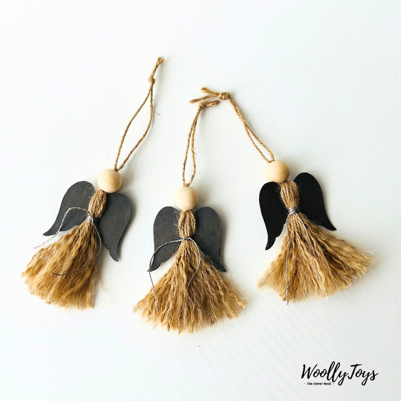 Három kézműves natúr angyal karácsonyfadísz ezüst szárnyakkal, spárgából és fából, egymás mellett fektetve, békés hangulatot árasztva.