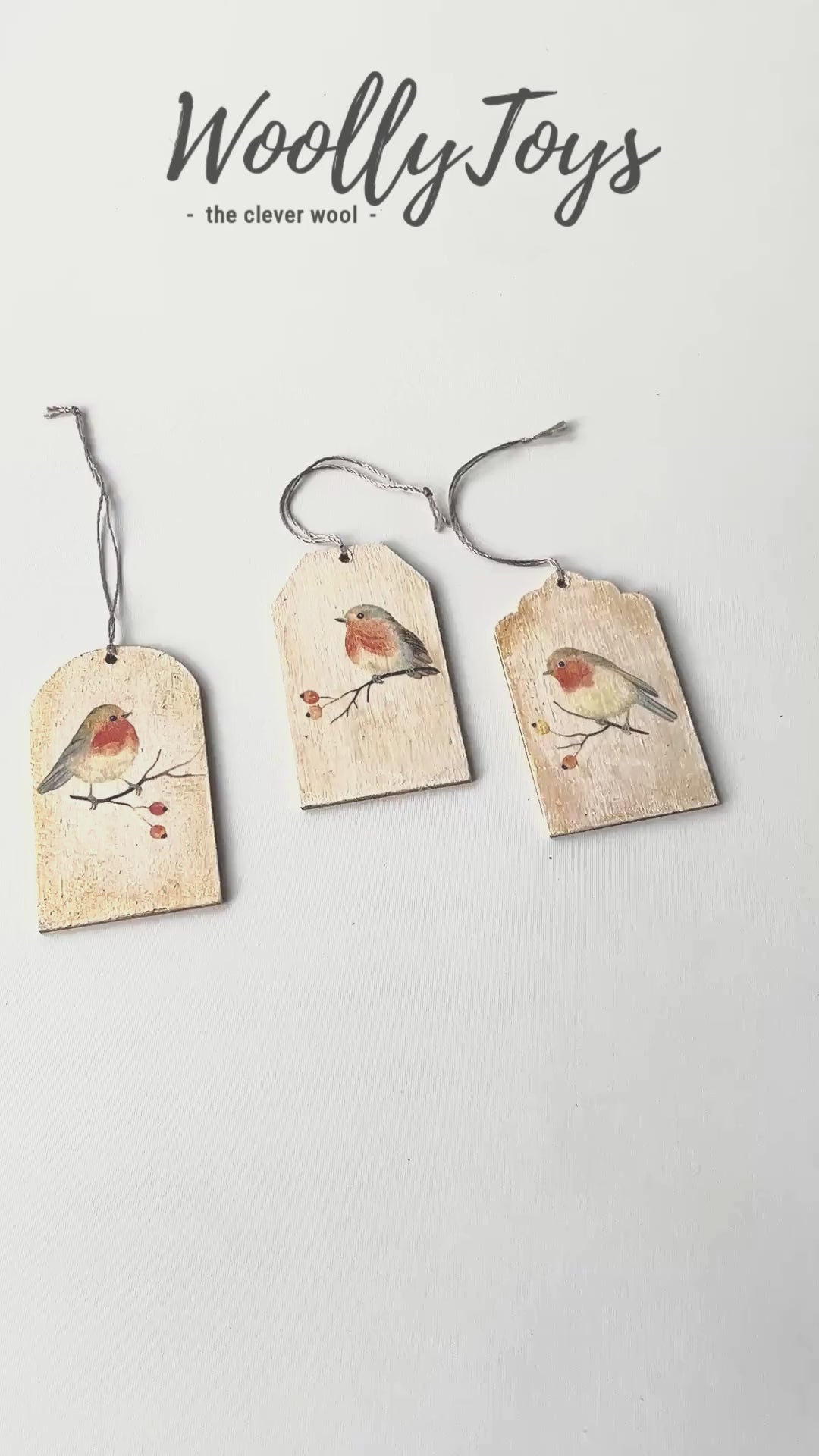 Videó, amelyen egy kéz mutatja be közelről a kézműves vörösbegy mintás fa ajándékkísérőt, kiemelve a szalvéta technika és a fa erezetének részleteit.