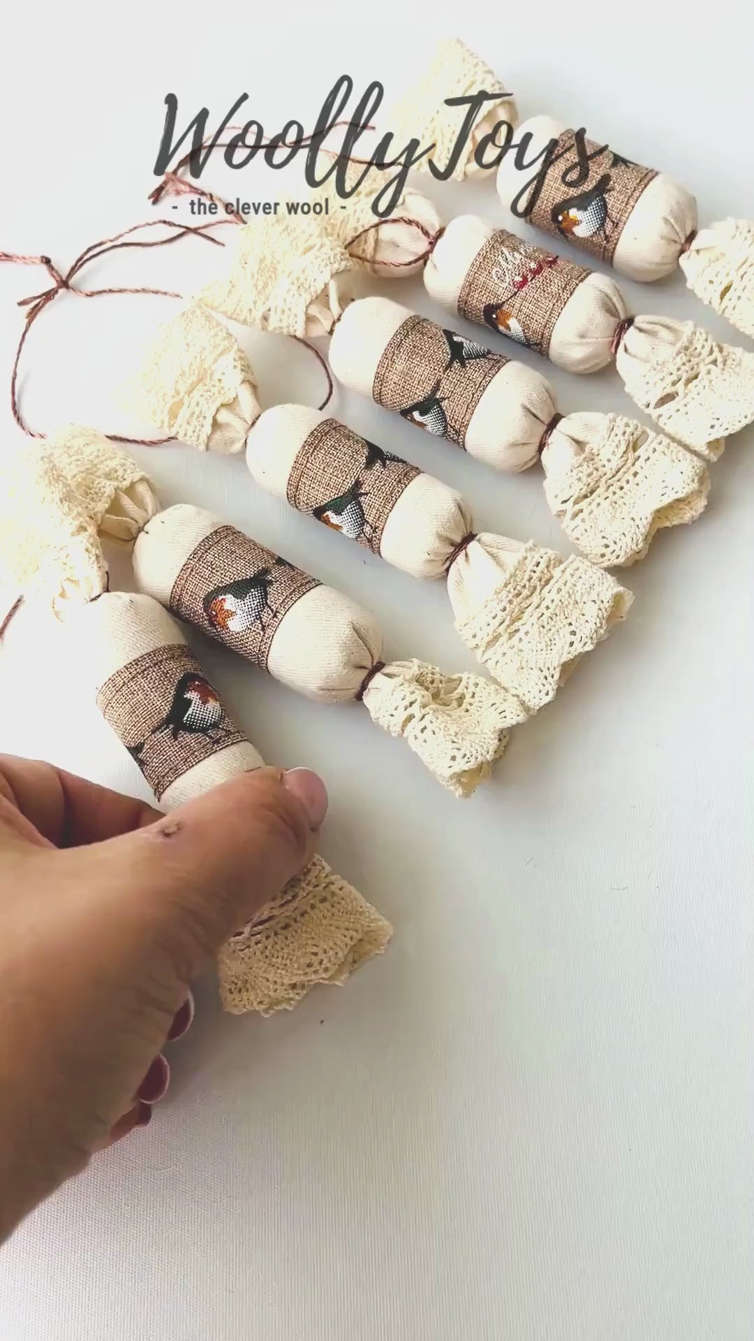 Videó, amelyen egy kéz mutatja be a kézműves vörösbegy mintás textil szaloncukor karácsonyfadísz minden oldalát, kiemelve a textúrát és a részleteket.