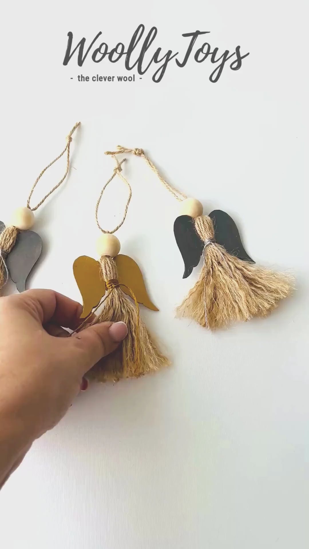 Videó, amelyen egy kéz mutatja be közelről a kézműves natúr angyal karácsonyfadíszt arany szárnnyal, kiemelve a spárga részleteit és a fa golyó fejet.