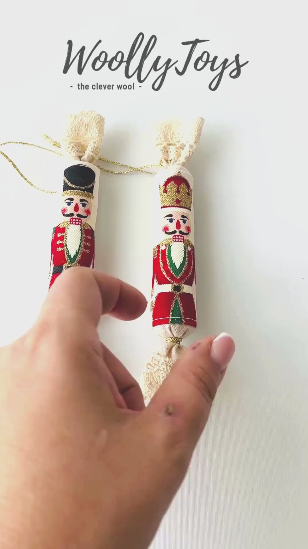 Videó, amelyen egy kéz mutatja be a kézműves textil piros kalapos diótörő mintás szaloncukor minden oldalát, kiemelve a mintát és az arany zsinórt.