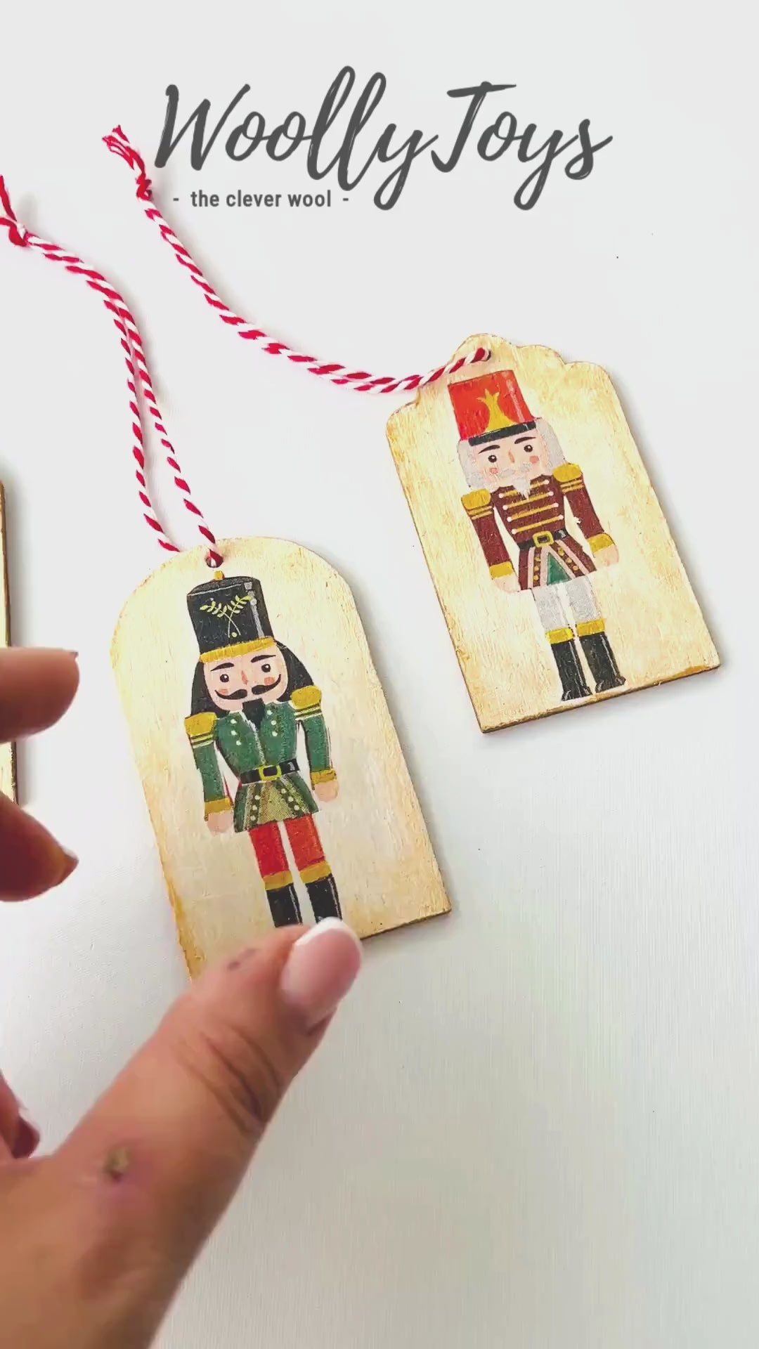 Videó, amelyen egy kéz mutatja be közelről a kézműves diótörő mintás fa ajándékkísérőt, kiemelve a szalvéta technika és a fa erezetének részleteit.