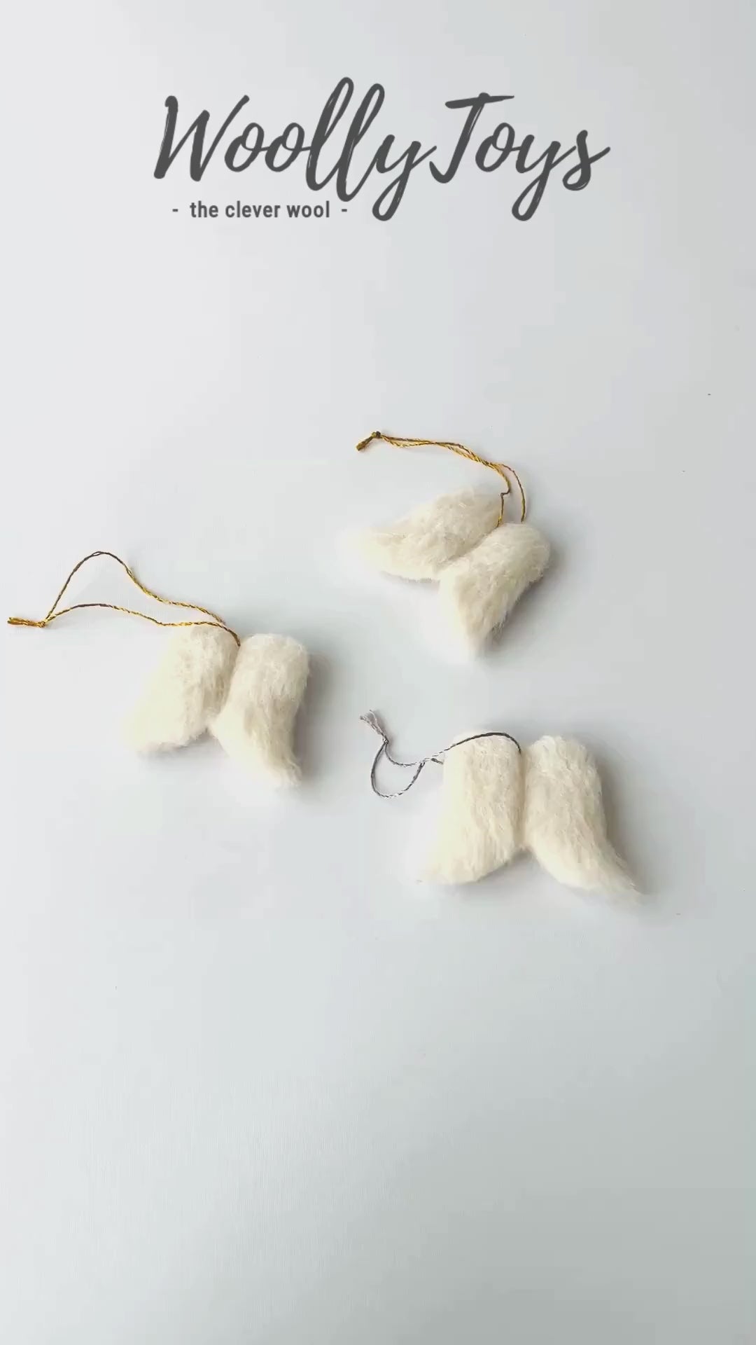 Videó, amelyen egy kéz mutatja be a fehér kézműves gyapjú  angyalszárny karácsonyfadísz minden oldalát, kiemelve a finom textúrát és a gravírozható fa hátoldalt.