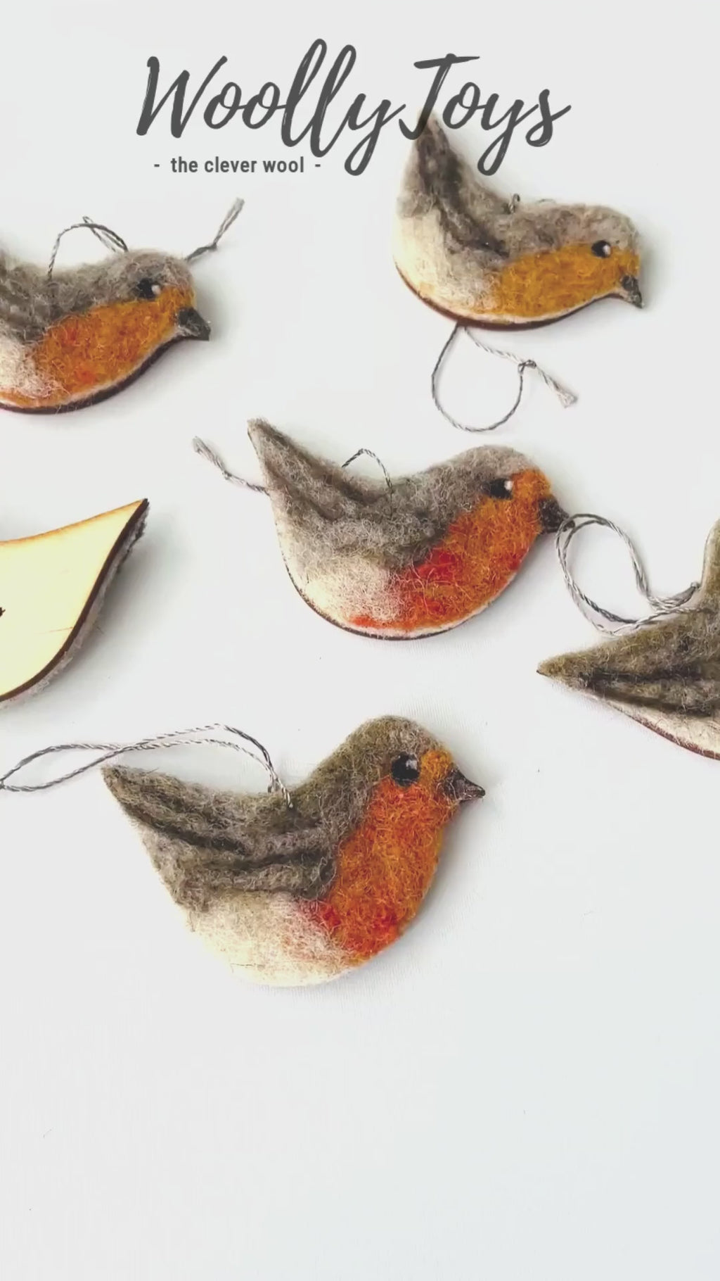 Videó, amelyen egy kéz mutatja be a kézműves tűnemezelt szines gyapjú vörösbegy karácsonyfadísz minden oldalát, kiemelve a finom textúrát és a gravírozható fa hátoldalt.