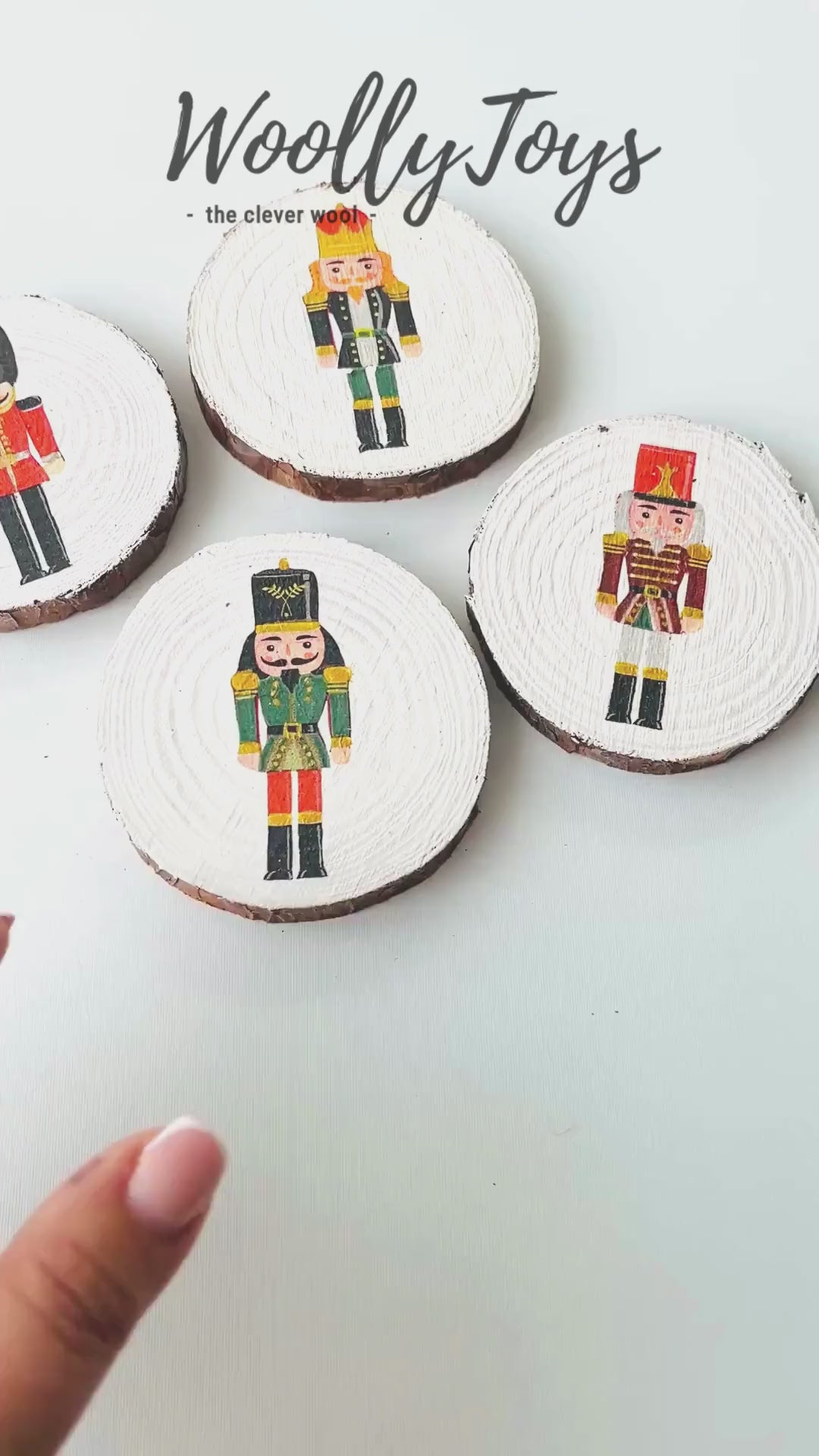 Videó, amelyen egy kéz mutatja be a kézműves szines diótörő mintás fa poháralátétet minden oldalról, kiemelve a szalvéta technikát és a gravírozható fa hátoldalt.